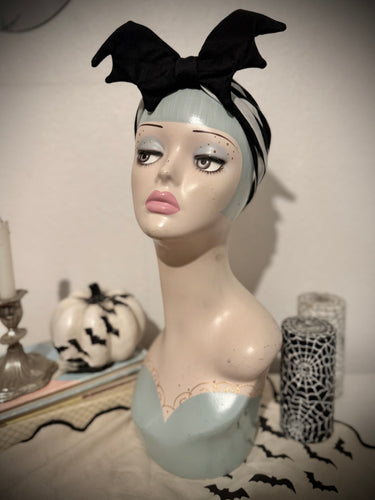 Mannequin head with a black bat halloween headband on a neutral background