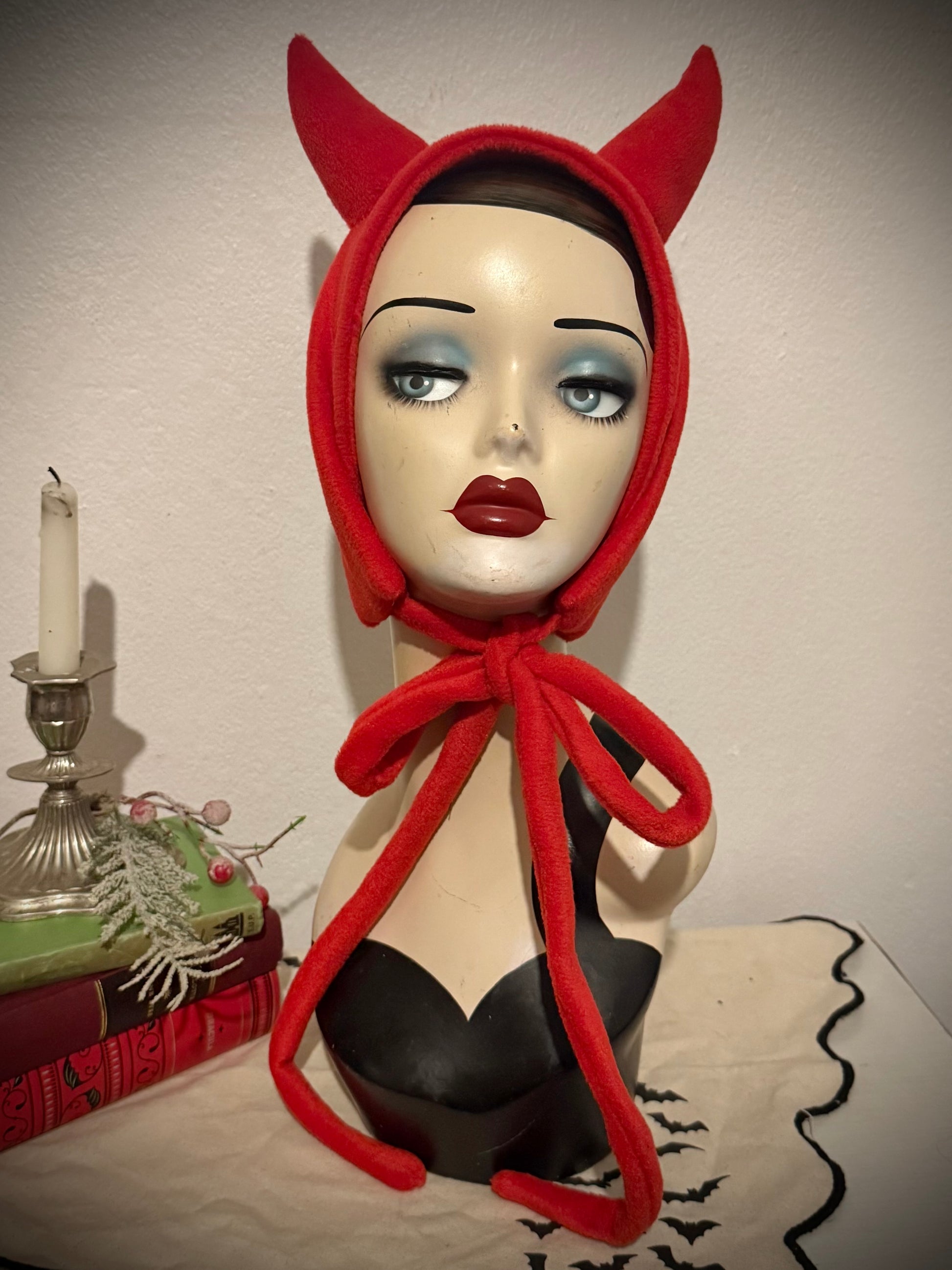Mannequin head wearing a red devil horn headband with a candle and decorative items in the background.
