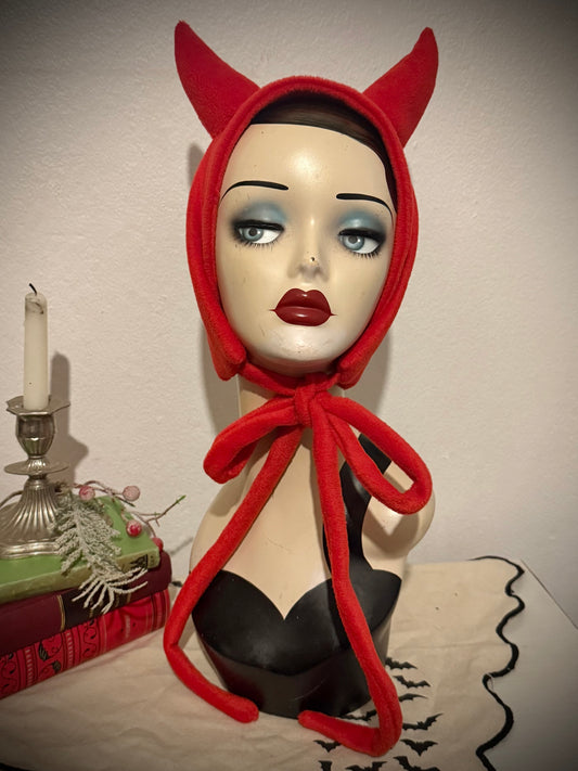 Mannequin head wearing a red devil horn headband with a candle and decorative items in the background.