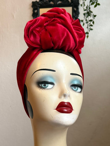 Mannequin head wearing a red velvet turban with a neutral background