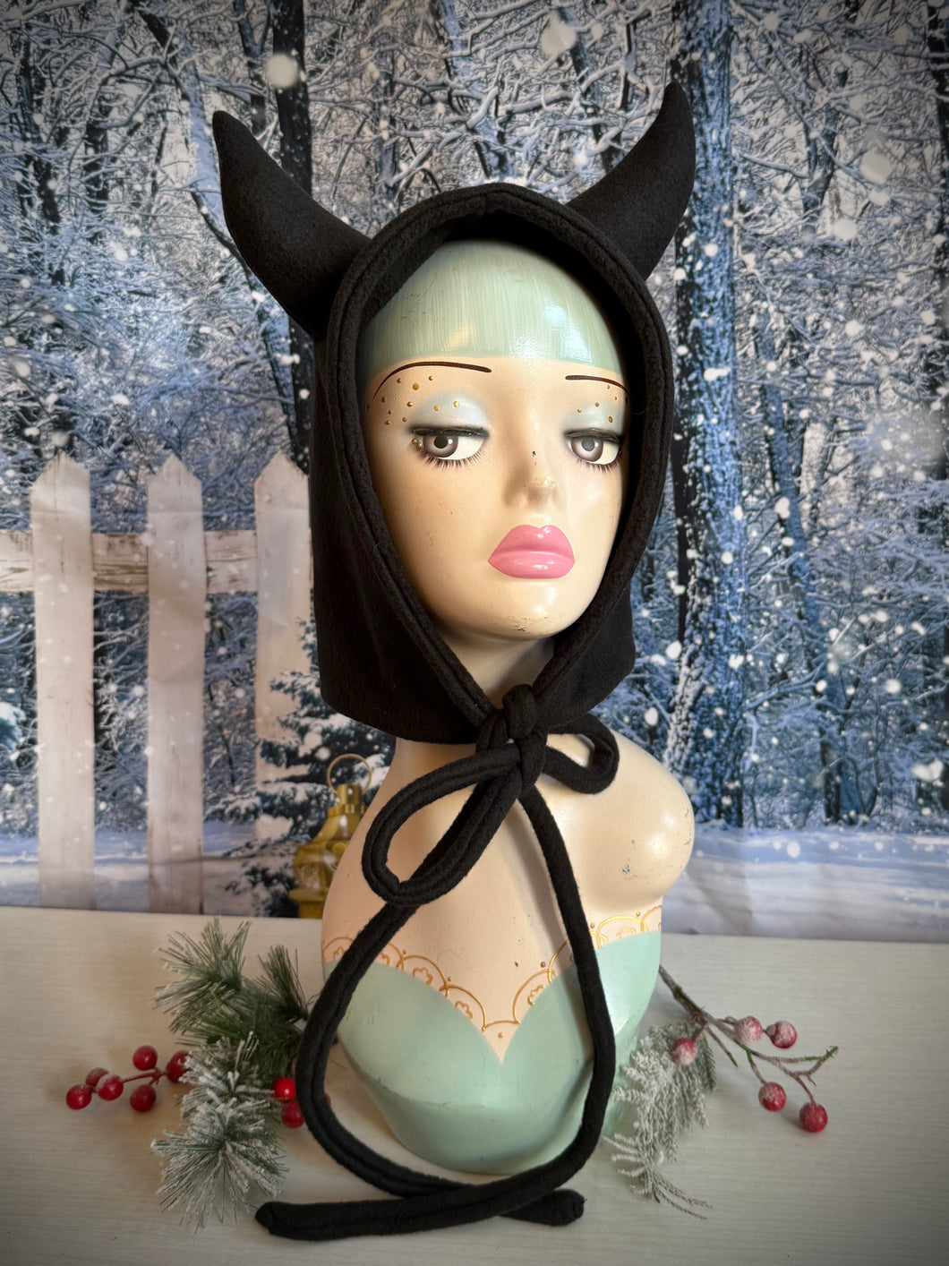 Mannequin head wearing a black devil horn Krampus hood against a snowy background