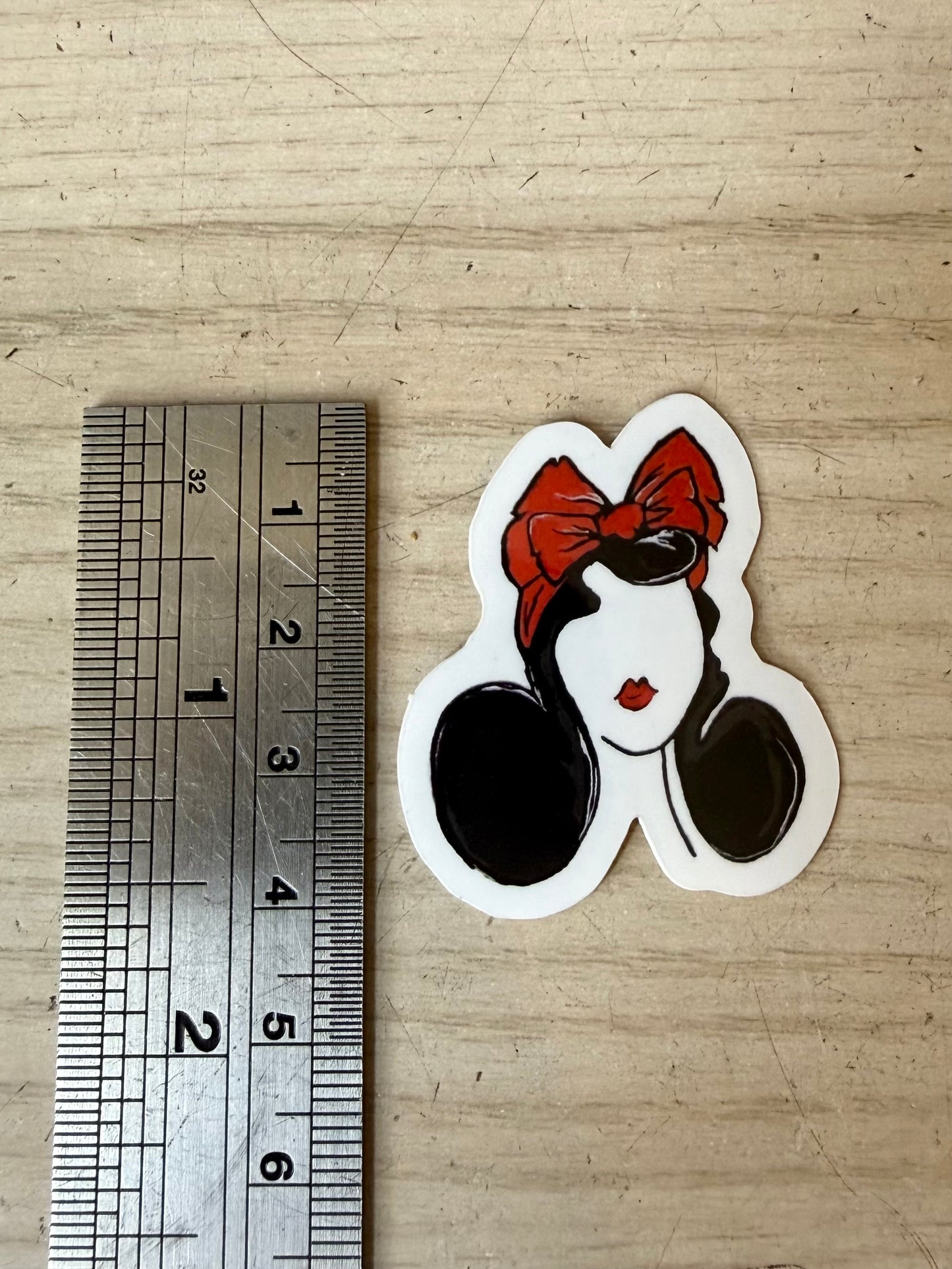 Sticker of a face with a red bow next to a ruler on a wooden surface