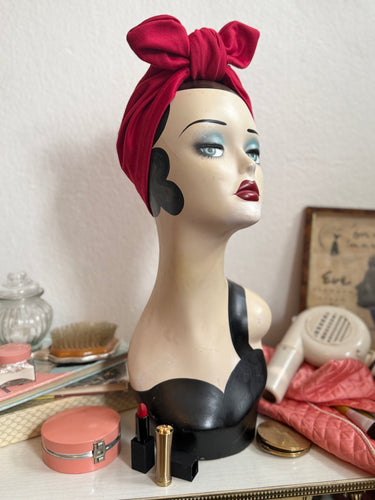Vintage display head on a dressing table full of make-up wearing a glamorous red 1940s turban