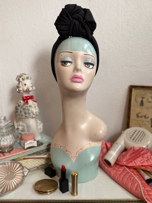 Vintage display head wearing a glamorous black handmade headband on a dressing table full of vintage make up