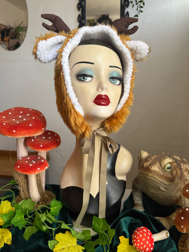 Fawn headpiece. Mannequin head with a deer-like costume in a decorative setting with mushrooms and plants.